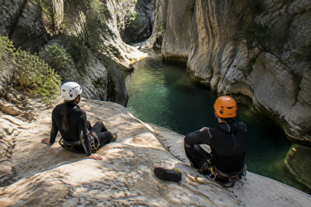 Canyoners resting on sunlit rocks above a deep green pool