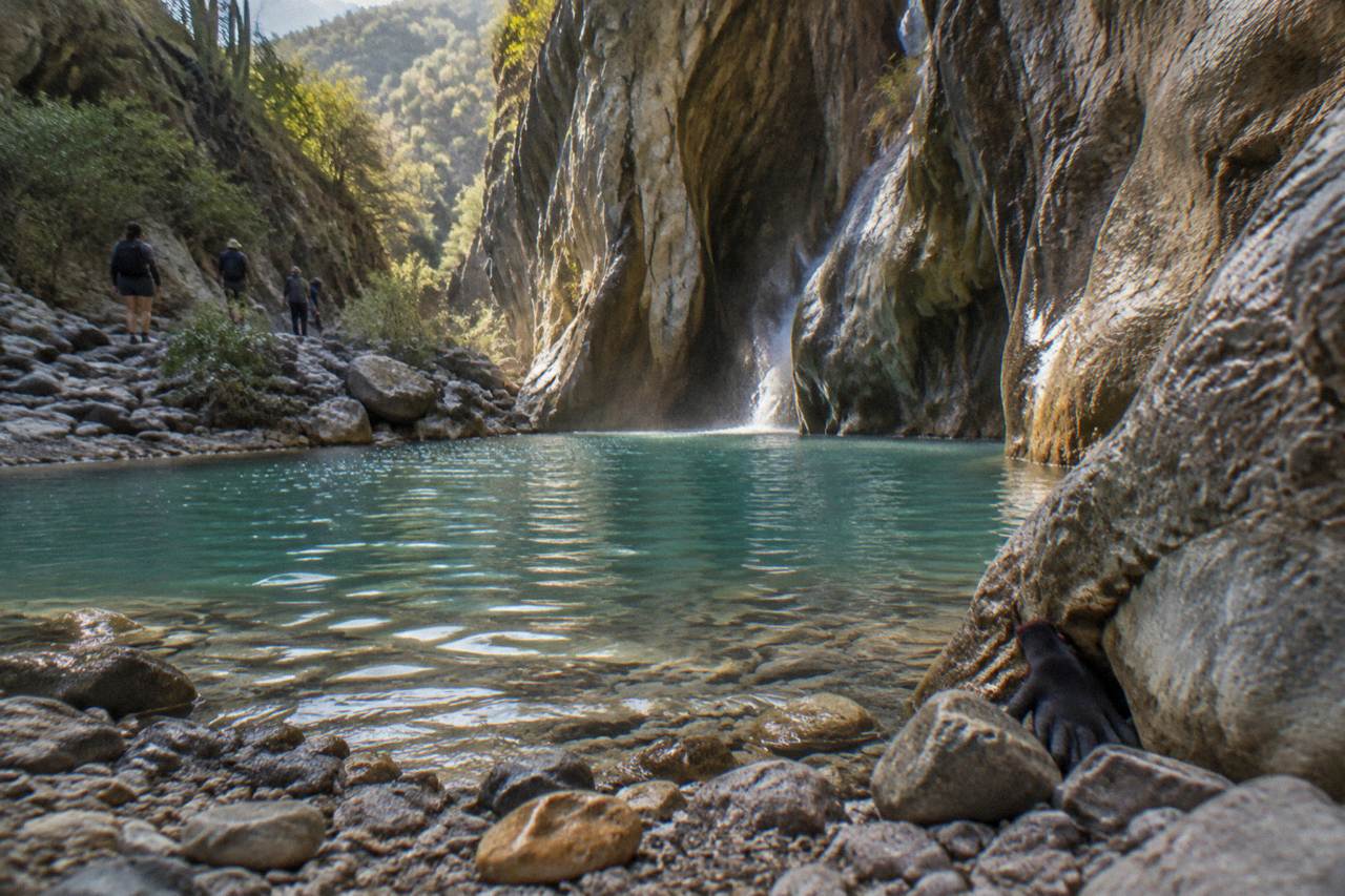 Turquoise pool at the base of a narrow limestone canyon with waterfall spray