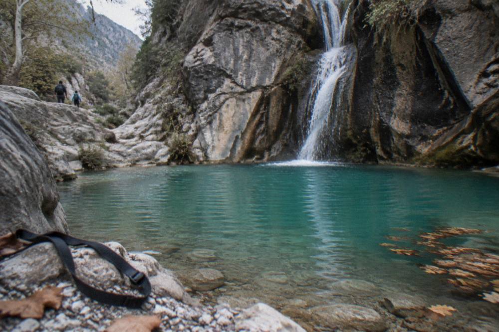 Turquoise pool at the base of a canyon waterfall framed by dark rock walls