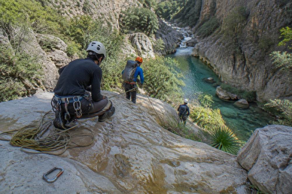 Line of canyoners rigged on ropes at the top of a rock drop in a green canyon
