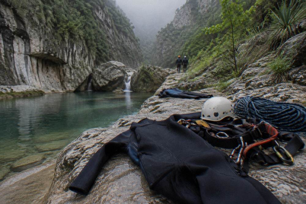 Wetsuits helmets and harnesses laid out on rock beside a canyon pool