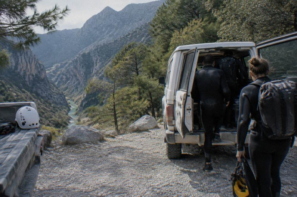 Group of hikers in wetsuits boarding a 4x4 van at a mountain trailhead