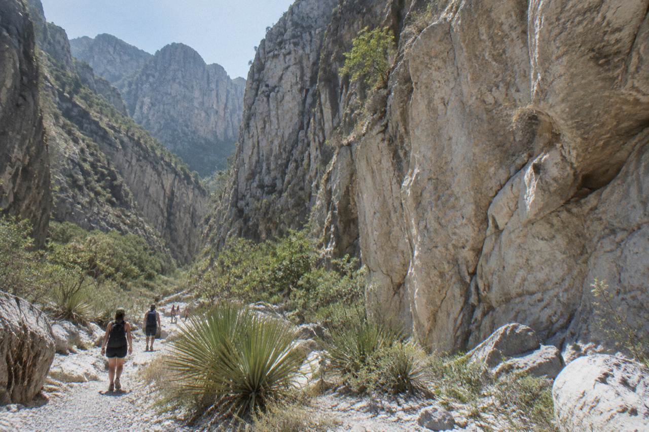 Limestone canyon walls rising above dry scrubland under a wide blue sky