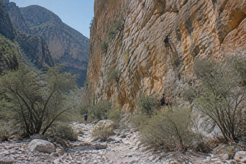 Orange limestone cliffs of Potrero Chico rising above a dry canyon floor with scattered shrubs