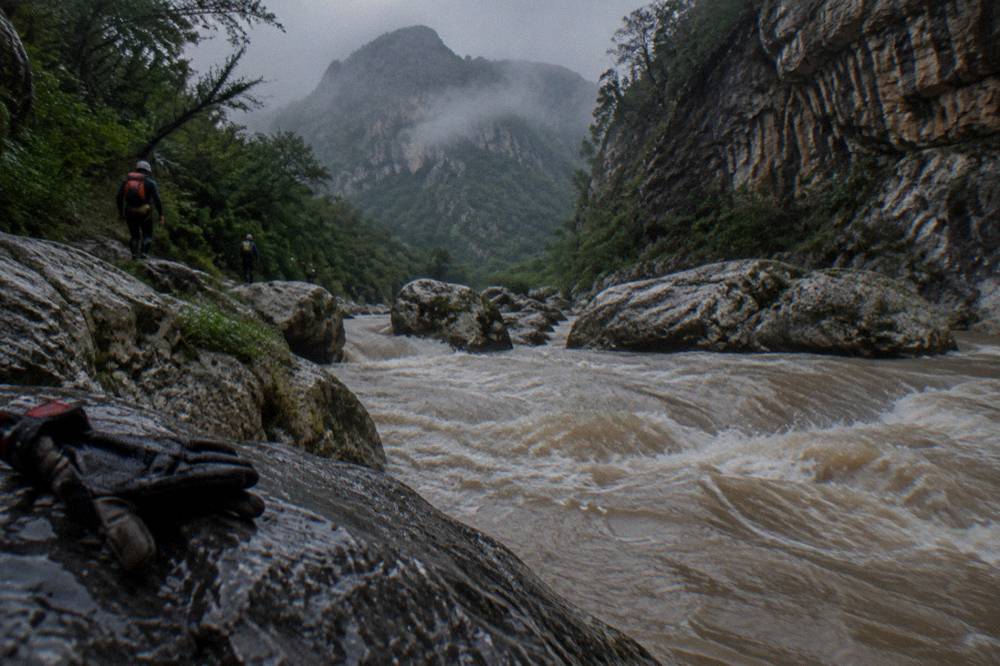 A rain-swollen mountain river rushing between boulders under overcast skies in the Sierra de Santiago
