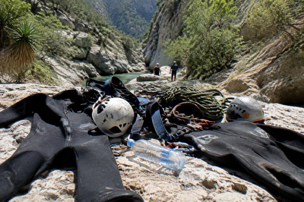 Canyon gear laid out on rock: wetsuits, helmets, harnesses and coiled ropes drying in sunlight