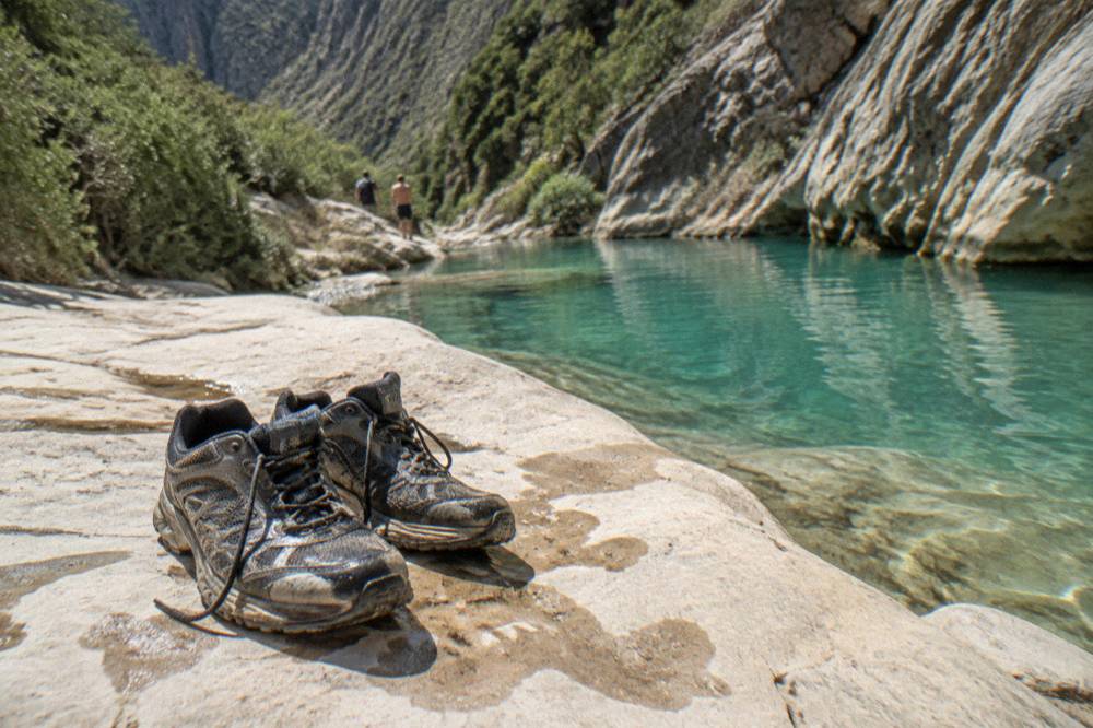 Worn trail shoes drying on a sunny rock next to a canyon pool