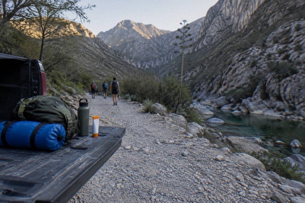 A small daypack with a dry bag, sunscreen and a water bottle on a tailgate