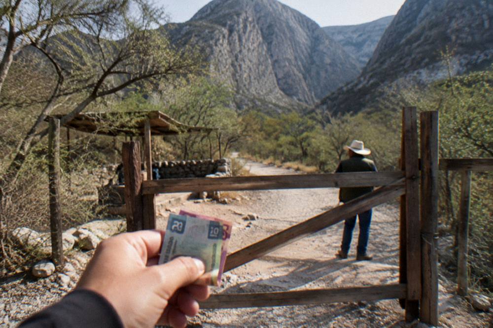 Pesos in small bills held out at a rural trailhead gate