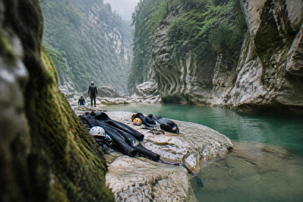 Canyoning gear laid out on a rock beside a turquoise pool in a narrow canyon