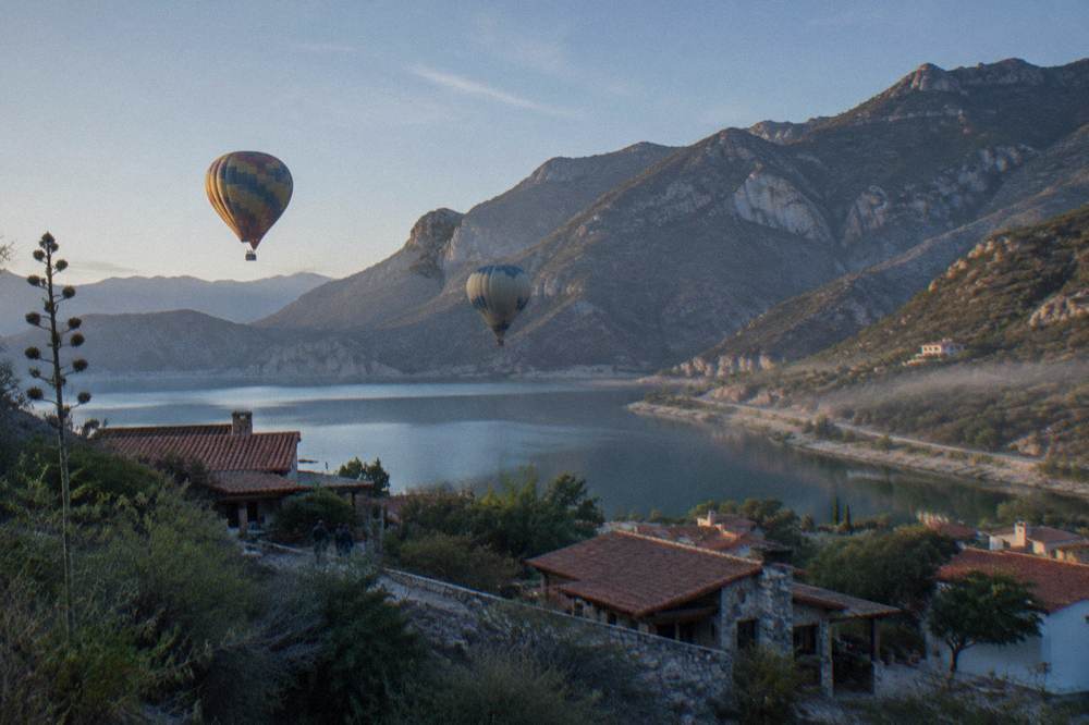Hot air balloons over a lakeside town surrounded by mountains at dawn