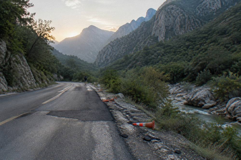 Empty two-lane highway winding through green hills at first light